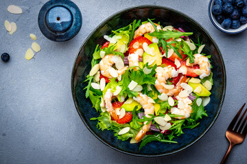 Foodie food salad with shrimp, strawberries, onion, arugula and almond petals, gray background, top
