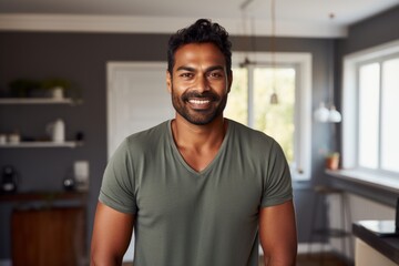 Portrait of a joyful indian man in his 30s dressed in a casual t-shirt while standing against scandinavian-style interior background