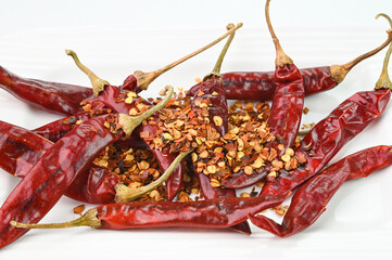 Red chilli peppers and chilli flakes on a plate.