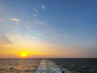 Beautiful sunrise over calm open sea, captured from a ferry boat. Golden light reflects on the water, with soft waves and vibrant sky, evoking tranquility and adventure at sea.