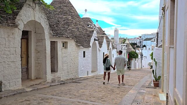 A couple enjoys a romantic stroll through the charming streets of Alberobello, Puglia, surrounded by the iconic trulli houses that define the scenic landscape of this area