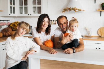 happy family preparing for Halloween celebration, they are in the kitchen and playing with pumpkins. The atmosphere is bright and cozy, surrounded by autumn decorations with bright leaves.