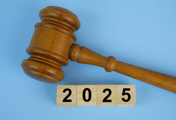 Wooden judge gavel and numbers 2025 on wooden cubes on blue background. Concept of laws in year...