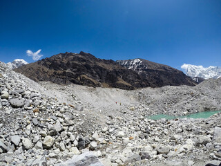 Side view of Ngozumpa glacier covered with ice and large stones and rocks in Himalayas in a sunny spring day. Small lake. Cholatse mountain peak in background. Unrecognizable people. Extreme terrain.