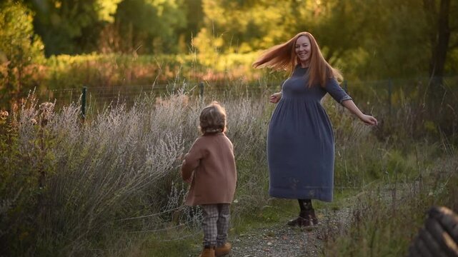 Mother and son spinning in autumn park, happiness and positive emotions, autumn leaves flying. Beautiful young woman, beautiful red hair, boy with blond curls, beautiful clothes, sunset, October
