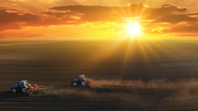 Aerial view of a farmers in two tractors seeding at sunset. Drone shot of sowing agricultural crops at field
