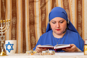 A Jewish woman teacher at a table wearing headphones conducts an online lesson on prayer