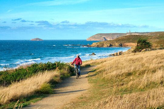 nice senior woman cycling with her electric mountain bike at the rocky emerald coast  of Brittany, France next to Cap Frehel