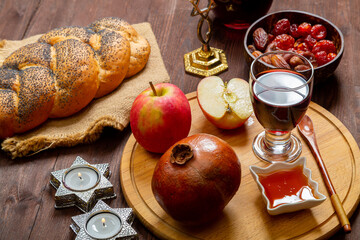 Challah, honey, apple and pomegranate and wine with burning candles on the table