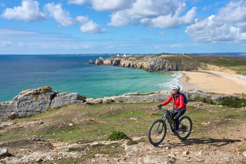 active senior woman cycling with her electric mountain bike along the  wild coast of Finisterre in...