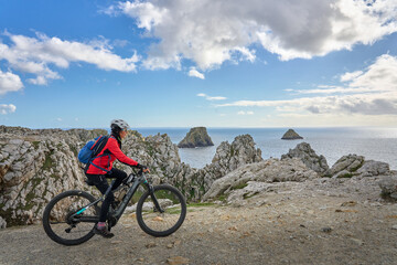 Obraz premium active senior woman cycling with her electric mountain bike along the wild coast of Finisterre in southern Brittany next to Camaret-sur-Mer, France
