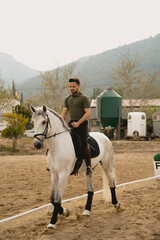 Portrait of a young rider on his white horse in the training arena. Vertical photo. Riding club concept