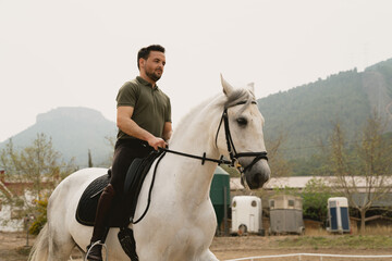 Portrait of a young rider on a white horse in an outdoor equestrian arena. The mountains behind. Equestrian Concept & Training