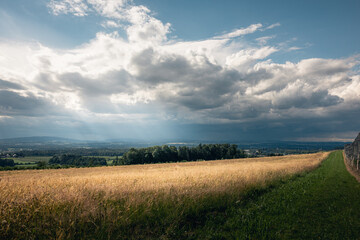 Weite Landschaft mit bewölktem Himmel und goldenen Feldern unter dramatischem Licht