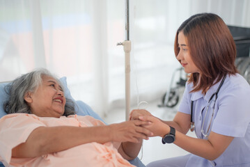 Happy young Asian female nurse gives encouragement to senior woman patient at the hospital ward