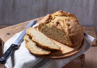 Homemade Irish soda bread cut into pieces and knife on wooden background.