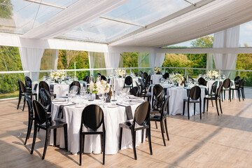 Served tables decorated with flowers in a restaurant on an open veranda with a fabric canopy. Preparations for receiving guests. Banquet in honor of the bride and groom