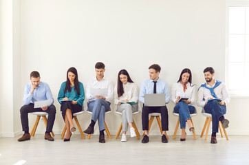 Obraz premium Happy different business people sitting on office chairs in row line, smiling diverse job seekers chatting, waiting for hr interview, human resource staff group team portrait, businesspeople