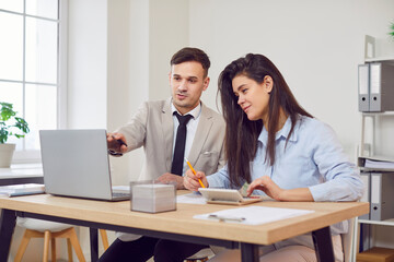 Serious business people at table busy doing office expenses management, use calculator to calculate, learning to pay bills through secure e-banking app on laptop, study finances and accounting help