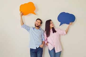 Portrait of a confident smiling couple holding empty colorful speech bubbles above their heads...