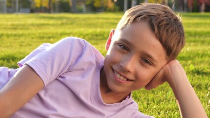 A happy, playful boy is lying on the grass in the park. The face of a joyful boy relaxing on a...