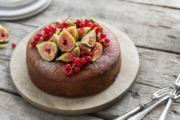 Whole fig cake with fresh sliced fruits and red currant served on wooden table