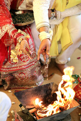A bride in traditional attire performs a sacred ritual, offering prayers to the holy fire during a Hindu wedding ceremony.
