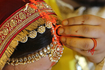 Indian wedding ritual where sindoor (vermilion) is being applied to the bride's hair parting, symbolizing the sacred bond of marriage.