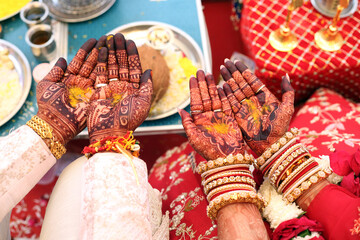 bride and groom's hands adorned with intricate henna designs and vibrant bangles, during a traditional Indian wedding ritual.