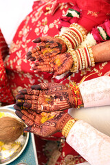 bride and groom's hands adorned with intricate henna designs and vibrant bangles, during a traditional Indian wedding ritual.