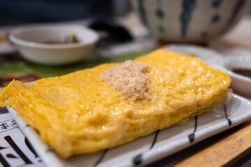 Closeup of a golden fluffy omelette or egg roll topped with fish dashi floss served on a ceramic plate in an Asian Japanese restaurant