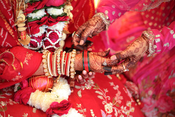 Indian wedding moment, with hands adorned in intricate henna designs, vibrant red bangles, and...