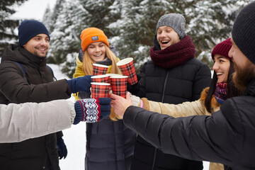 Happy smiling friends relaxing, clinking a glass of hot coffee among snow covered trees in snowy...