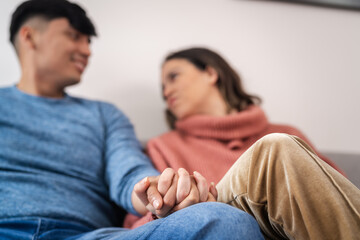 Young couple holding hands sitting on sofa at home