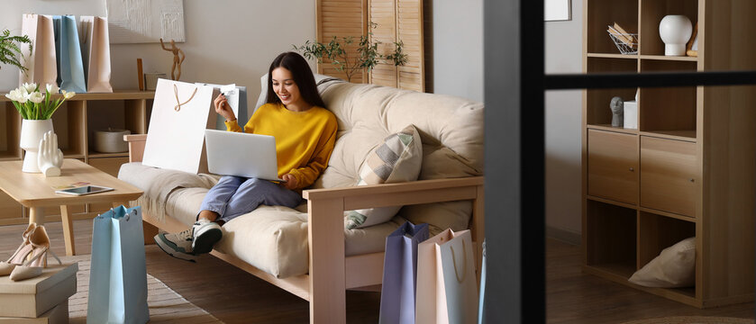 Young Asian woman with laptop and credit card shopping online at home