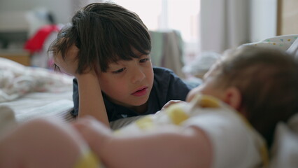 Older sibling lying on a bed, gazing intently at their baby sibling. The quiet moment reflects the bond and affection shared between the two in a warm, intimate setting