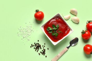 Bowl with tomato paste and fresh vegetables on green background