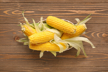 Wicker bowl with fresh corn cobs on wooden background
