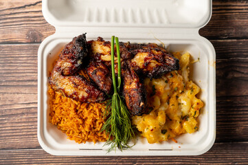Caption: Tasty Caribbean food served on a white plate or white bowl on a rustic vintage wooden table backdrop - colorful home cooked meals and desserts with chicken, chips, vegetables, rice, bbq, stew