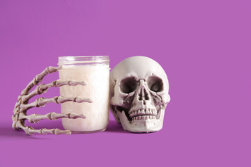 Glass of milk, skull and skeleton hand for Halloween on purple background