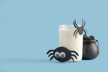 Glass of milk, bowl and spiders for Halloween on blue background