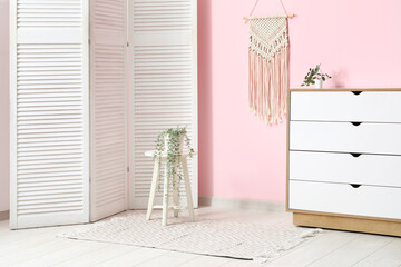 Interior of living room with chest of drawers, houseplant on stool and stylish rug