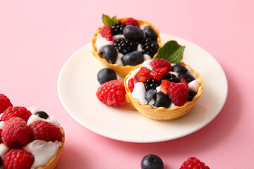 Plate of tasty tartlets with whipped cream and berries on pink background