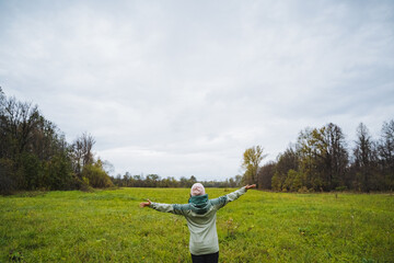 A woman stands in a vast, sprawling field with her arms wide open, embracing the fresh air around her, feeling deeply connected to the vibrant greenery and beauty of nature surrounding her