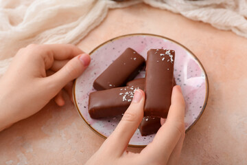 Woman eating tasty chocolate covered coconut candies on beige background