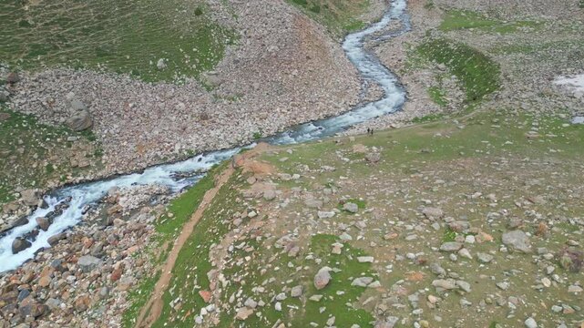 Aerial shot of a rugged rocky mountain trail winding alongside a pristine river in the breathtaking landscape of Kaghan Valley, Pakistan.