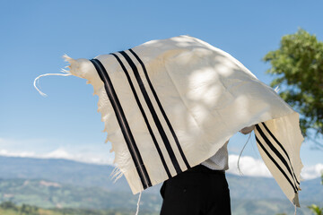 Young Jewish Man Draping the Tallit Over His Body Outdoors Under Blue Sky