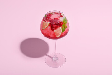 Glass of fresh raspberry mojito on pink background