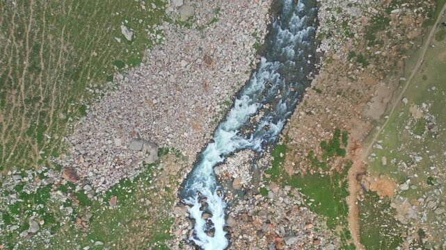 Aerial shot of a rugged rocky mountain trail winding alongside a pristine river in the breathtaking landscape of Kaghan Valley, Pakistan.