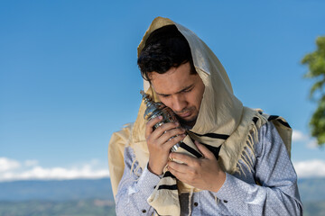 Young Jewish Man Embracing a Sefer Torah Under His Tallit with a Blue Sky Background